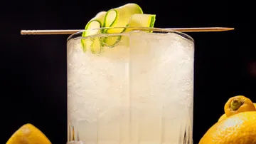 Cucumber cocktail garnished with lemon slices, dark background.