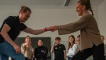 Two people dancing, group watching in room.