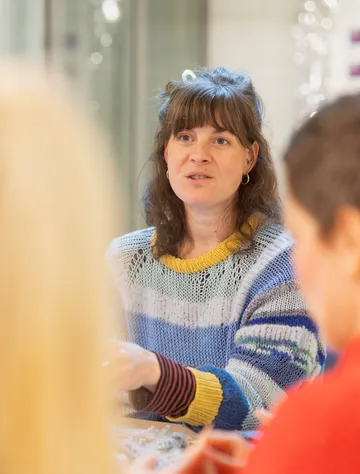Woman in colorful sweater speaking at table.