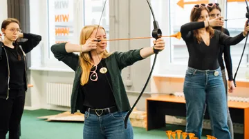 Vier Frauen üben drinnen Bogenschießen.