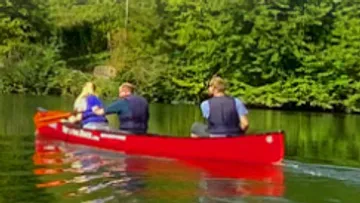 Drei Personen beim Kanufahren auf einem ruhigen Fluss.
