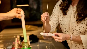 Woman decorating candle with paint, craft table.