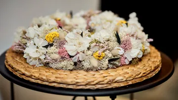 Floral wreath with white, pink, and yellow flowers on woven mat.