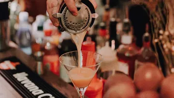 Cocktail being poured into a glass at bar.