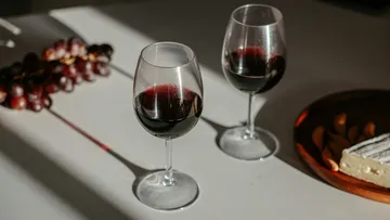 Two wine glasses with red wine, grapes nearby.