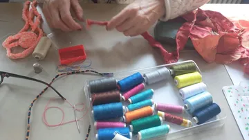 Hände, die mit Garn und Nähmaterial arbeiten.
