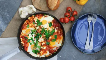 Shakshuka in a skillet, with bread and vegetables.