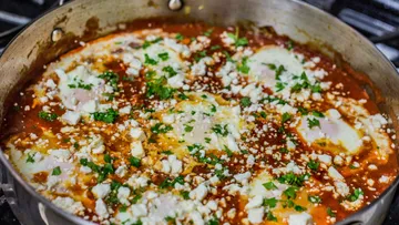 Shakshuka mit Eiern, Feta und Kräutern in einer Pfanne.