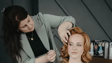 Stylist, der drinnen die roten Haare einer Frau kräuselt.
