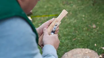 Person, die im Freien mit einem Handwerkzeug Holz schnitzt.