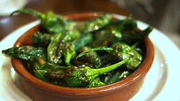 Roasted green peppers in brown dish.