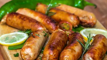 Grilled sausages on a wooden board with herbs.