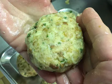 One hand holds a shaped, cooked dumpling in the kitchen.