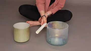 Person, die Kristallklangschalen mit einem Hammer spielt.
