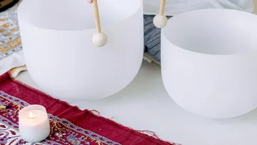 Zwei Klangschalen mit Schlägeln auf einem gemusterten Tuch.