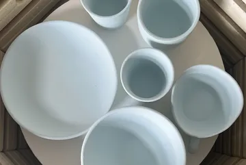 Weiße Keramikbecher und Schale auf rundem Tisch.