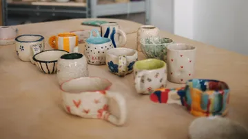 Bunte Keramikbecher auf einem Holztisch.