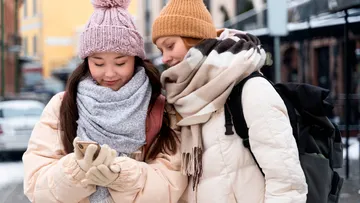 Zwei Frauen in Winterkleidung schauen draußen aufs Telefon.