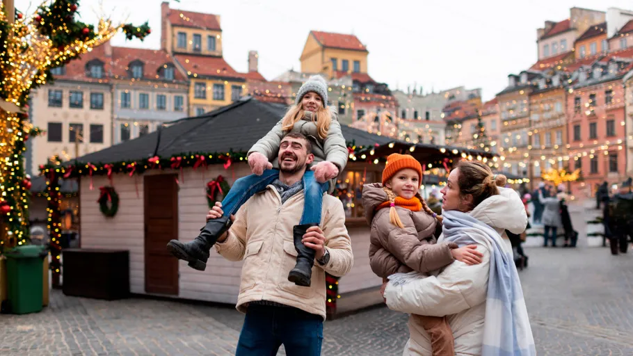 Family enjoying festive market with lights, stalls.