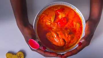 Hands holding a bowl of red stew.