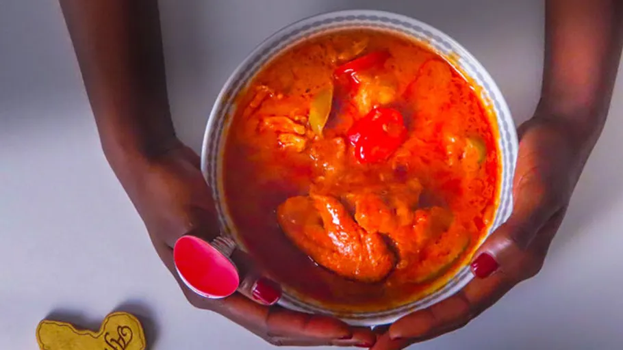 Hands holding a bowl of red stew.