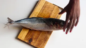 Fische von Hand auf ein Holzschneidebrett legen.
