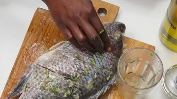 Fische auf einem Holzschneidebrett von Hand würzen.