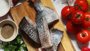 Roher Fisch auf einem Schneidebrett mit Tomaten.