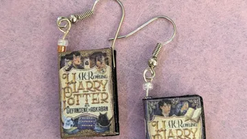Ohrringe mit Buchmotiven auf rosafarbener Oberfläche.