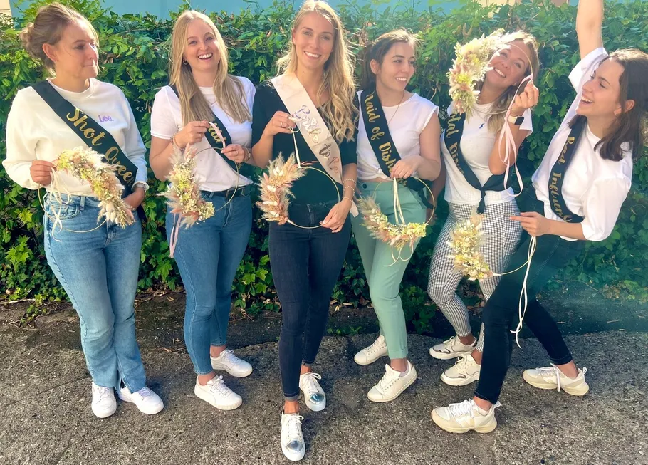 Gruppe von sechs Frauen, die im Freien mit Blumenkränzen feiern.