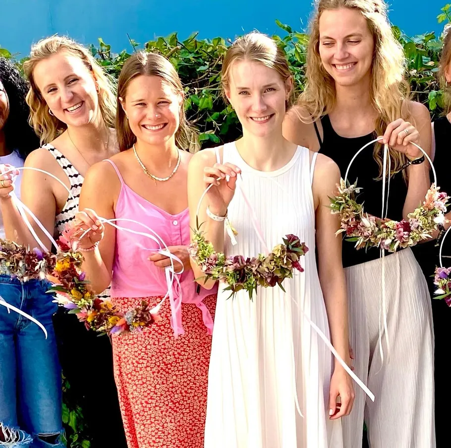 Vier Frauen, die Blumenkränze halten und draußen lächeln.