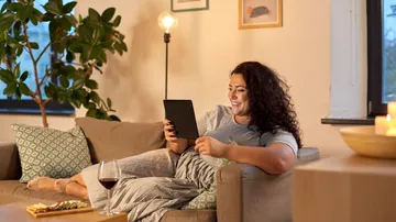 Woman reading on couch with tablet and wine.