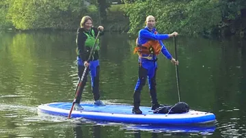 Zwei Personen paddeln auf einem ruhigen See.