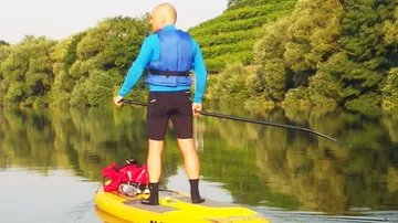 Person, die auf einem ruhigen Fluss mit Bäumen paddelt
