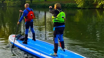 Zwei Personen paddeln auf einem ruhigen Fluss.