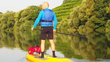 Person paddelt auf einem ruhigen Fluss, umgeben von Bäumen.