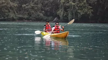 Two people kayaking on calm water near trees.