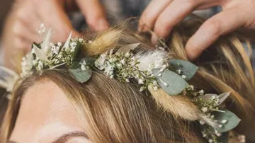 Hands adjust a floral wreath on hair.
