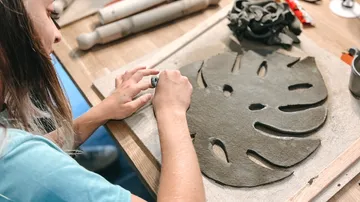 Person, die eine Monstera-Blattskulptur aus Ton herstellt.