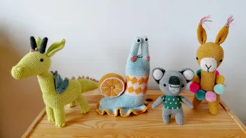 Gehäkelter Drache, Schnecke, Koala, Lama auf Holztisch.
