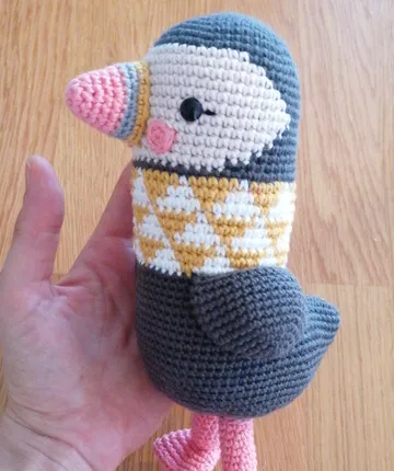 Handhaltendes gestricktes Papageientaucher-Spielzeug auf Holzboden.