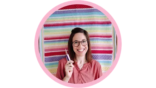 Lächelnde Person mit Häkelnadel, farbenfroher Garnhintergrund.