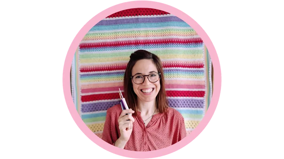 Smiling person holding crochet hook, colorful yarn backdrop.