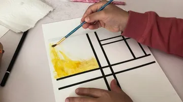 Person, die gelb auf geometrischem Muster malt.