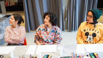 Three women sitting at a table with art supplies.