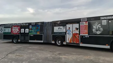 Langer schwarzer Bus mit diversen Werbeanzeigen auf der Seite.