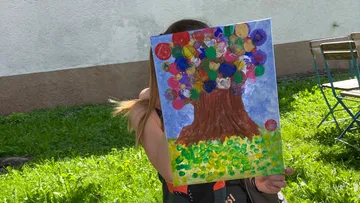 Person, die im Freien ein buntes Baumgemälde in der Hand hält.