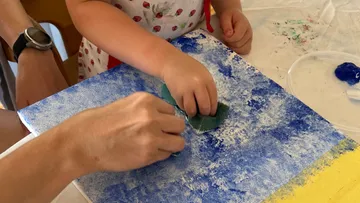 Child painting with sponge and blue paint.
