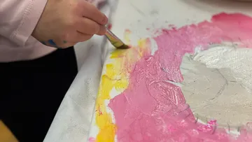Child painting with pink and yellow brush strokes.