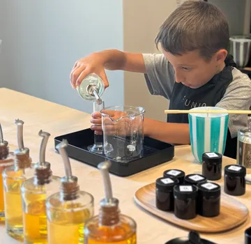 Child pouring liquid into a beaker on a table.